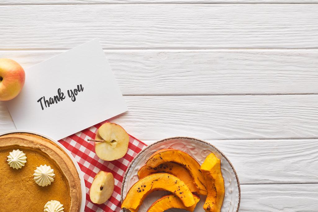 Top uitzicht van heerlijke pompoen taart met Bedankkaart op houten witte tafel met appels - Foto, afbeelding