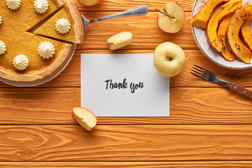 vista superior de delicioso pastel de calabaza, manzanas y tarjeta de agradecimiento en la mesa naranja de madera
 - Foto, Imagen