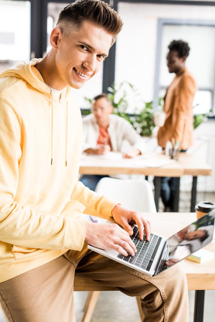nuori hymyilevä liikemies katselee kameraa työskennellessään lähellä monikulttuurisia kollegoja virassa
 - Valokuva, kuva
