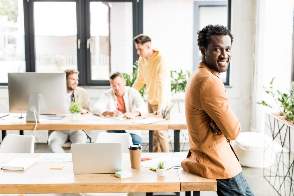 empresário afro-americano alegre olhando para a câmera perto de colegas que trabalham no escritório
 - Foto, Imagem