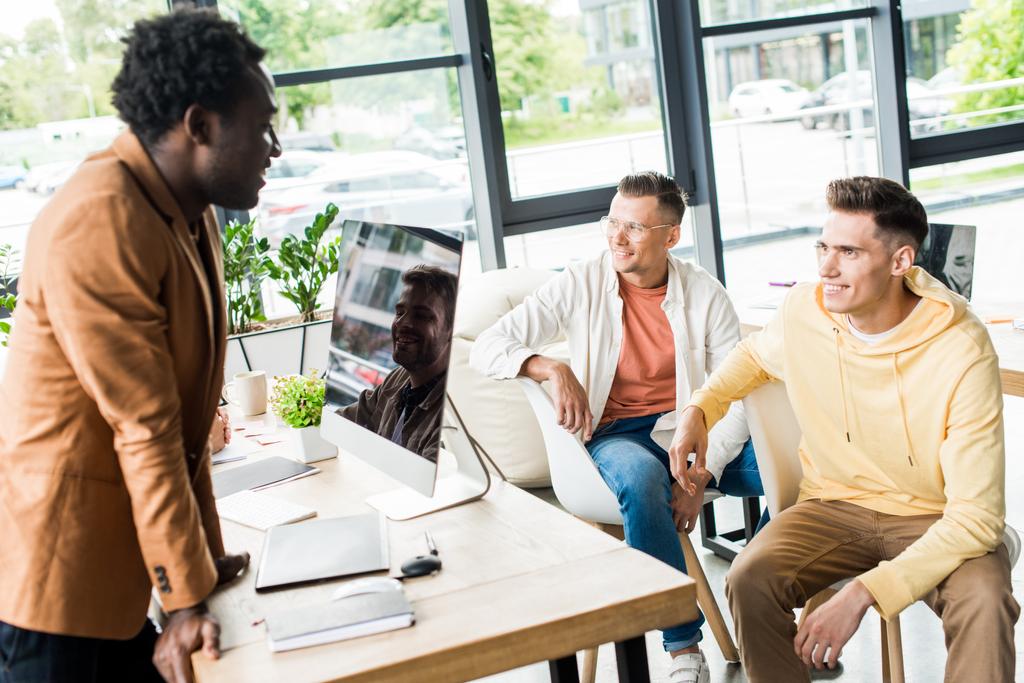 jonge, multiculturele ondernemers in gesprek over opstartprojecten op kantoor in de buurt van de werkplek met computermonitor - Foto, afbeelding