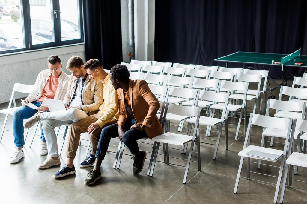 cuatro jóvenes empresarios multiculturales discutiendo el proyecto de startup mientras están sentados en la sala de conferencias
 - Foto, imagen