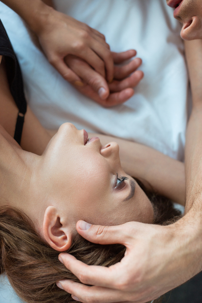 vrchní pohled na muže dotýkající tvář atraktivní dívky při ležení na posteli  - Fotografie, Obrázek