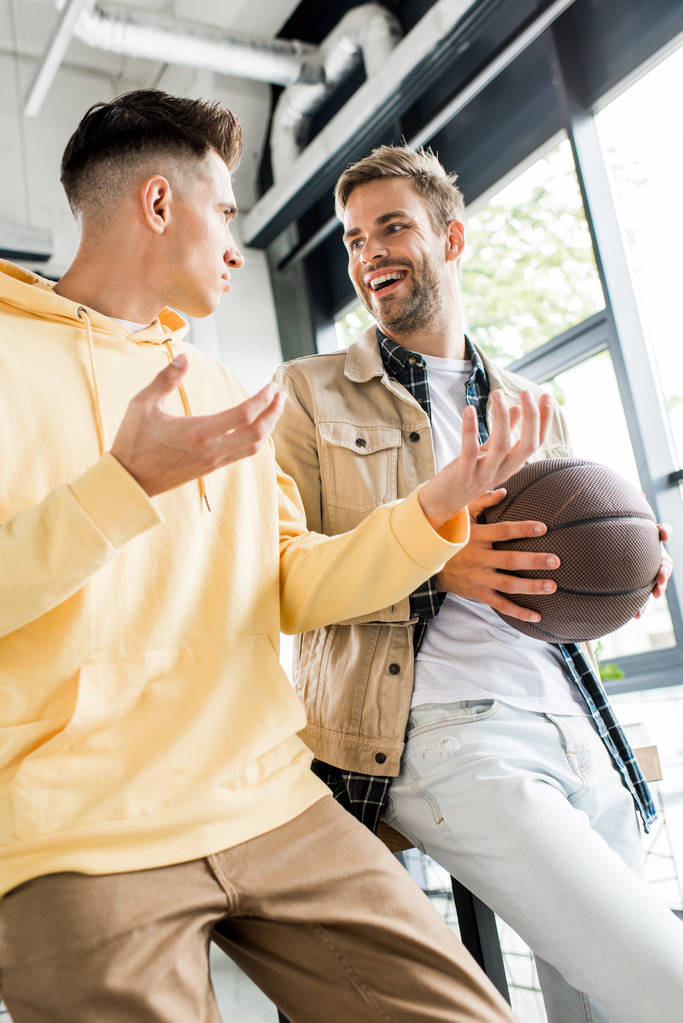 mladý podnikatel gestikuluje při rozhovoru s usměvavým kolegou držící volejbal  - Fotografie, Obrázek