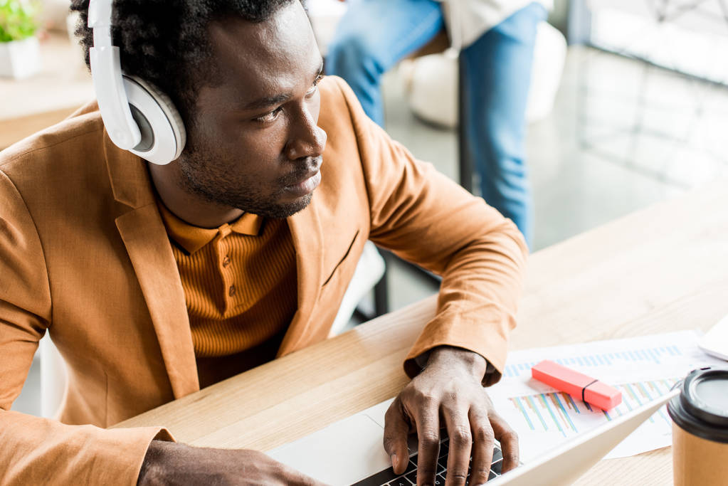 задумливий афроамериканський бізнесмен в навушниках, використовуючи ноутбук в офісі
 - Фото, зображення