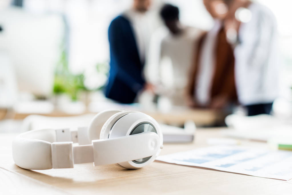 enfoque selectivo de los auriculares en el escritorio cerca de los empresarios de pie en el lugar de trabajo en la oficina
 - Foto, imagen