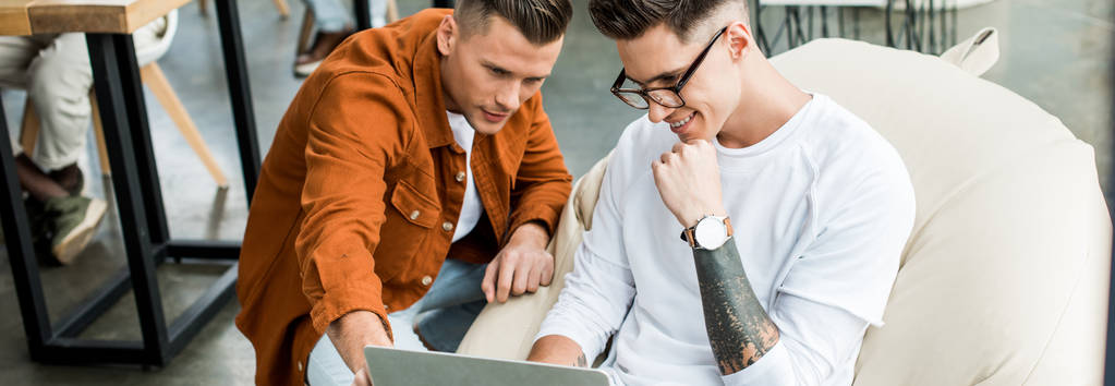 panoramisch schot van jonge zakenmannen op zoek naar laptop tijdens het werken aan startup project samen - Foto, afbeelding