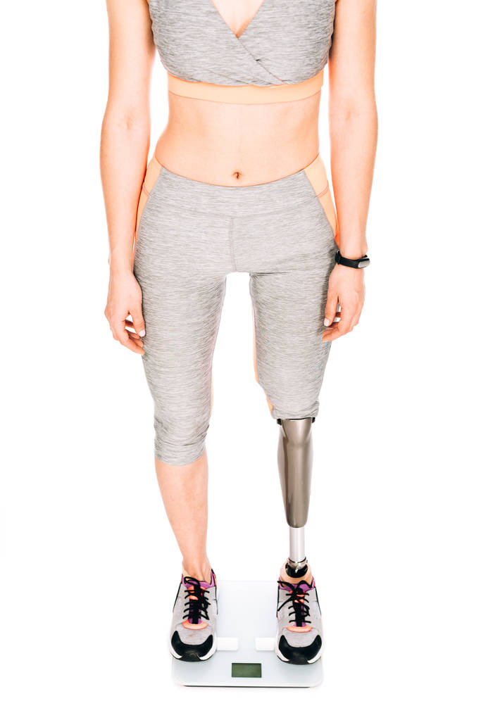 Teilaufnahme einer behinderten Sportlerin mit Beinprothese auf einer Waage isoliert auf weiß - Foto, Bild