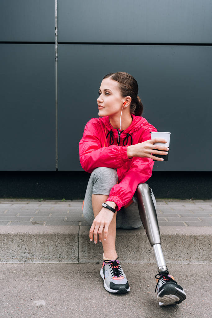 mozgássérült sportnő zenét hallgat fülhallgató és holding kupa az utcán - Fotó, kép