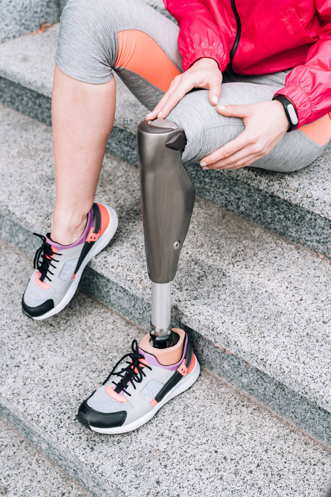 partial view of disabled sportswoman with prosthesis sitting on stairs - Photo, Image