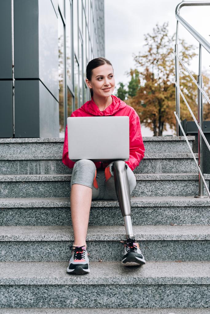 sportivo disabile che utilizza il computer portatile mentre seduto sulle scale sulla strada
 - Foto, immagini