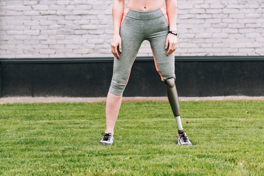 částečný pohled na postiženou sportovkyni s fitness trackerem na trávě - Fotografie, Obrázek