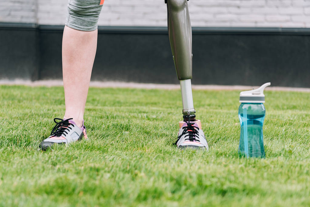 частковий вид на спортсменку-інваліда, що стоїть біля спортивної пляшки на траві на вулиці
 - Фото, зображення