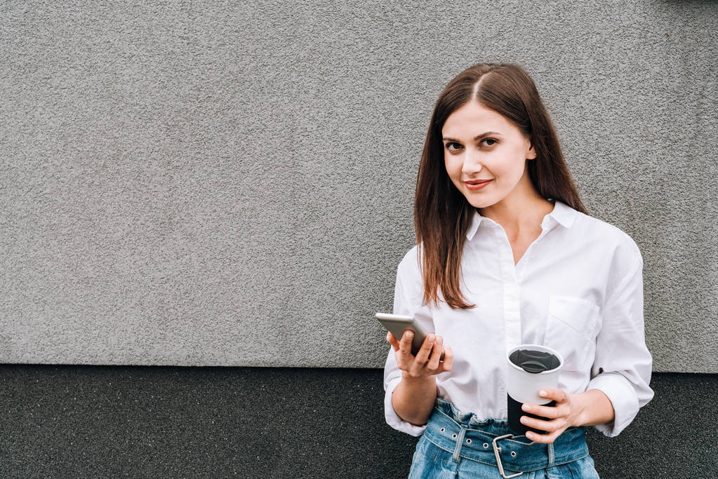 krásná mladá žena drží smartphone a šálek na ulici - Fotografie, Obrázek