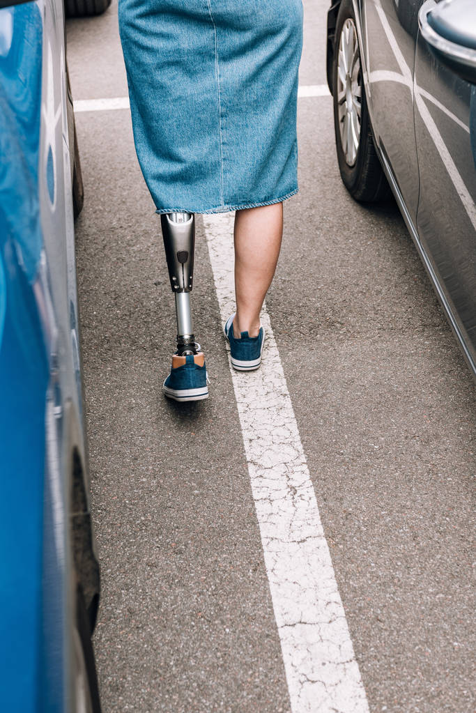 cropped view of disabled woman with prosthetic leg near cars on street - 写真・画像