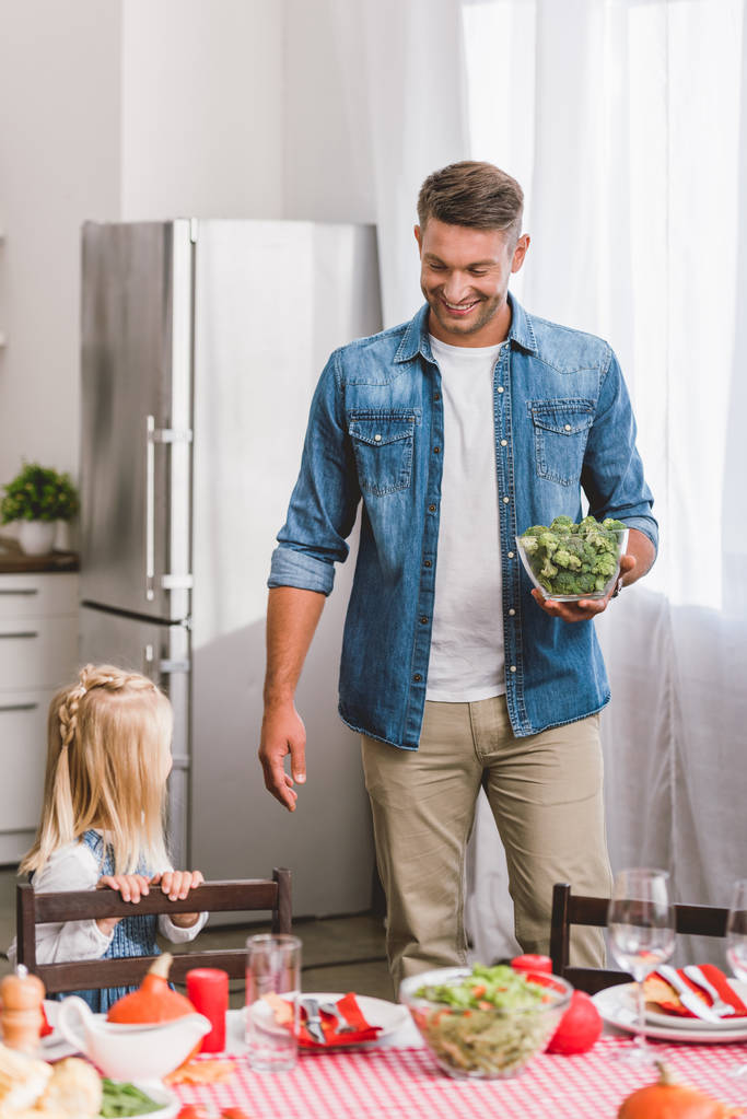 smiling father holding bowl with broccoli and looking at cute daughter in Thanksgiving day  - Photo, Image