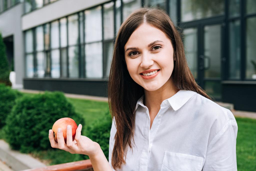 усміхнена приваблива молода жінка тримає яблуко на вулиці
 - Фото, зображення