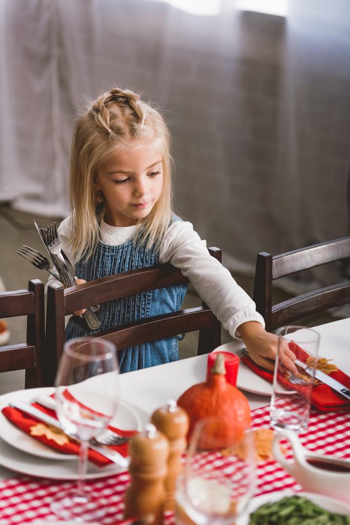Şükran Günü 'nde gülümseyen ve masaya çatal bıçak koyan sevimli bir çocuğun seçici odağı.   - Fotoğraf, Görsel