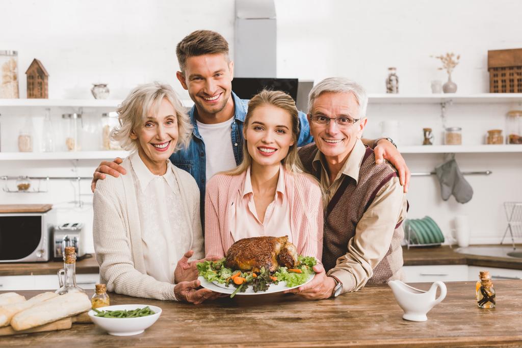 uśmiechnięci członkowie rodziny trzymając talerz z smacznym indykiem w Święto Dziękczynienia   - Zdjęcie, obraz