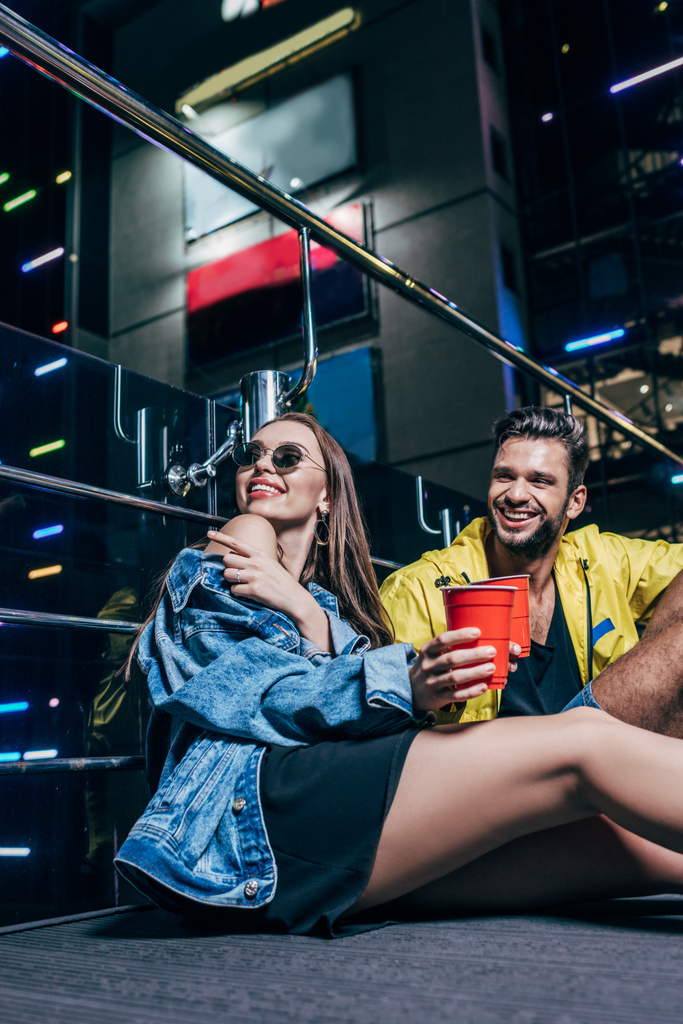 handsome boyfriend with plastic cup and attractive girlfriend pointing with finger in night city  - Photo, Image