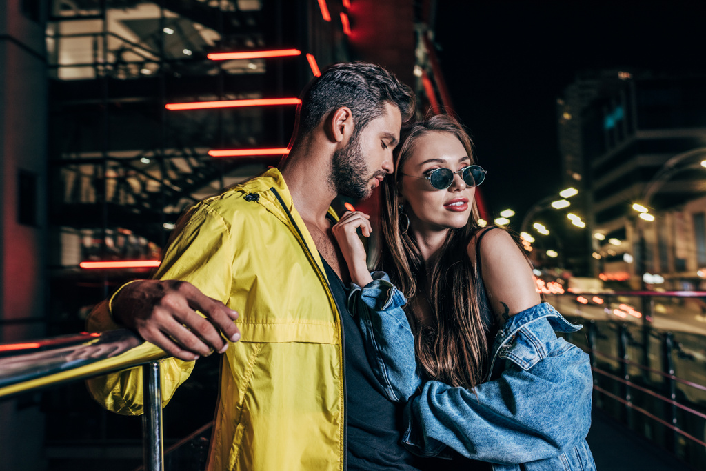 knappe vriendje en aantrekkelijke vriendin in denim jasje knuffelen in Night City  - Foto, afbeelding