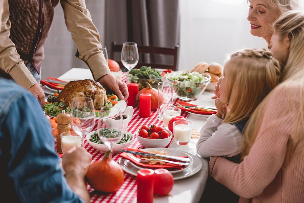 perheenjäsenet istuvat pöydässä ja isoisä tilalla lautasella kalkkunan kanssa kiitospäivänä
       - Valokuva, kuva