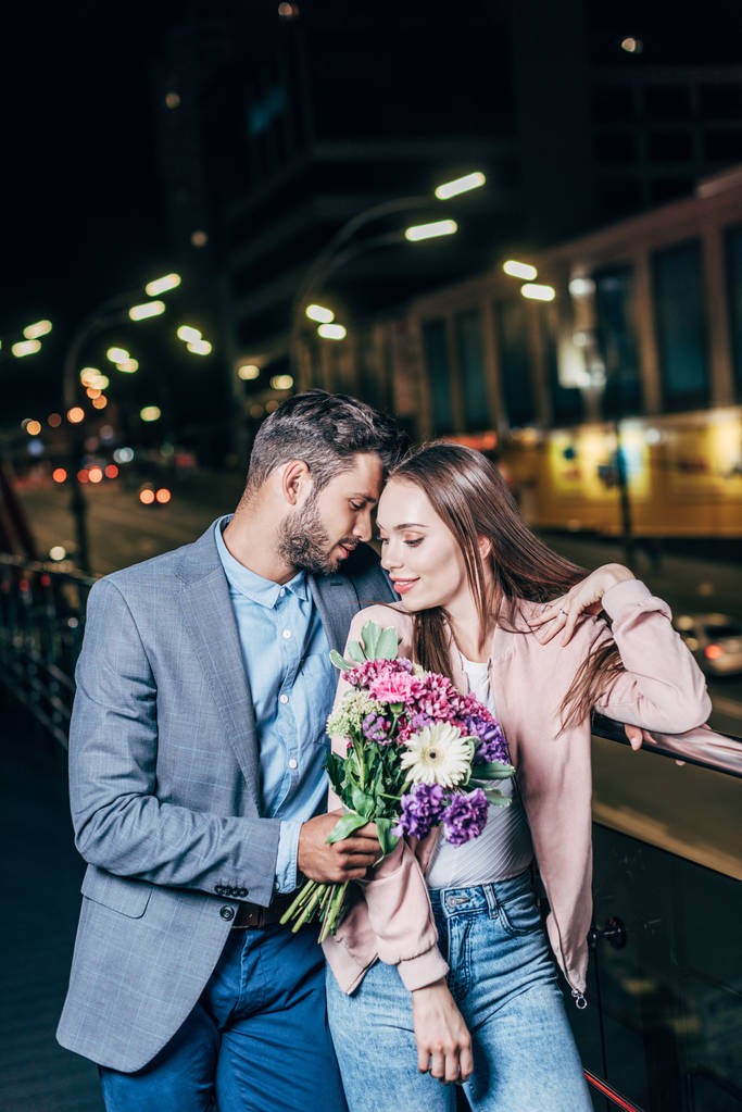красивый бизнесмен дарит букет и обнимает привлекательную женщину в ночном городе
  - Фото, изображение
