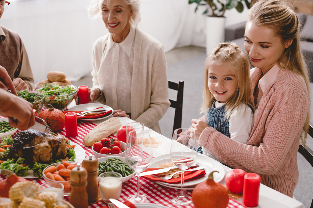 bijgesneden beeld van familieleden zitten aan tafel en vader snijden smakelijke kalkoen in Thanksgiving dag       - Foto, afbeelding