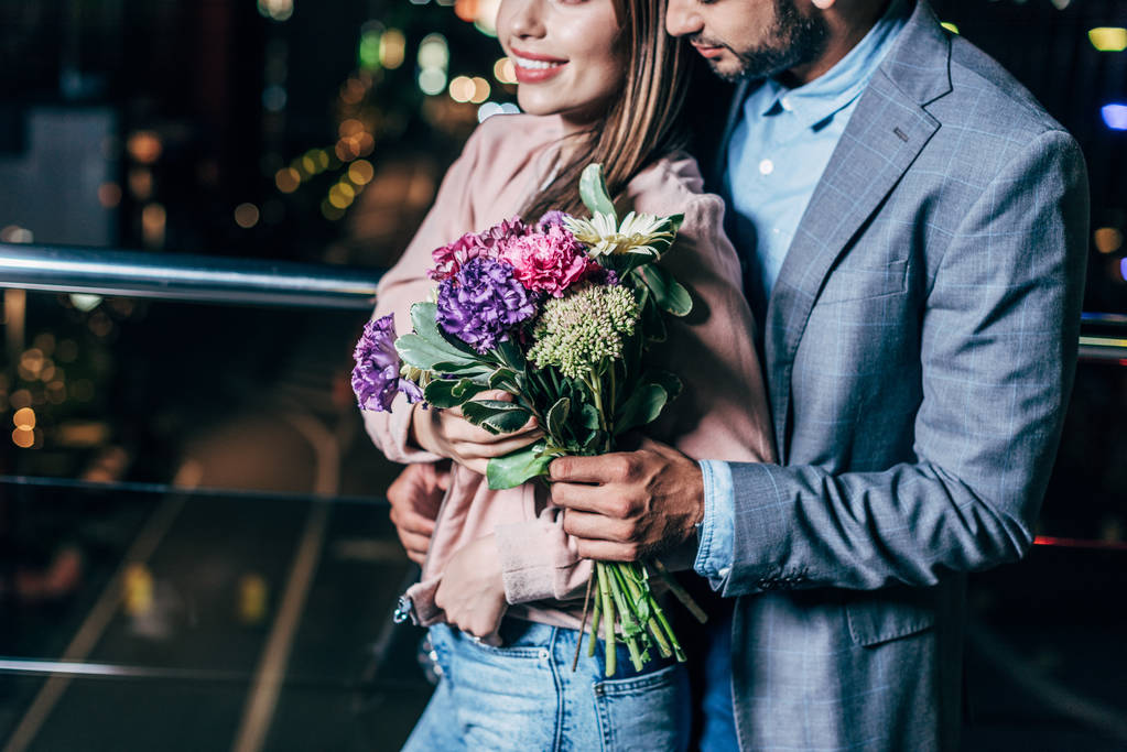 vue recadrée de l'homme d'affaires donnant bouquet et étreinte femme souriante dans la ville de nuit
  - Photo, image