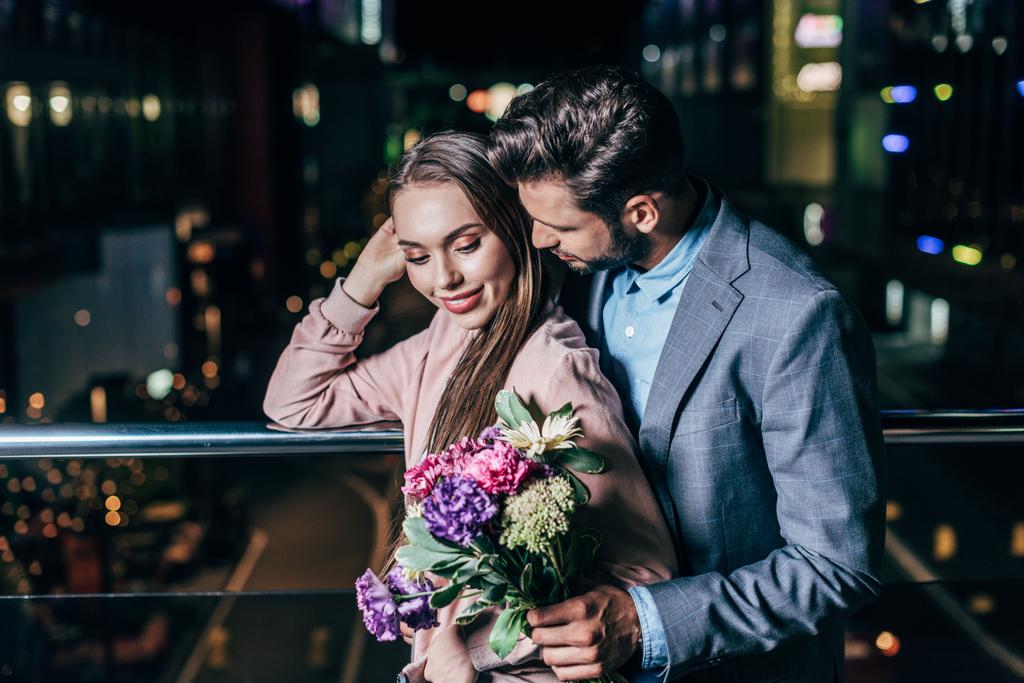 schöner Geschäftsmann gibt Blumenstrauß und umarmt attraktive Frau in der Nacht Stadt  - Foto, Bild