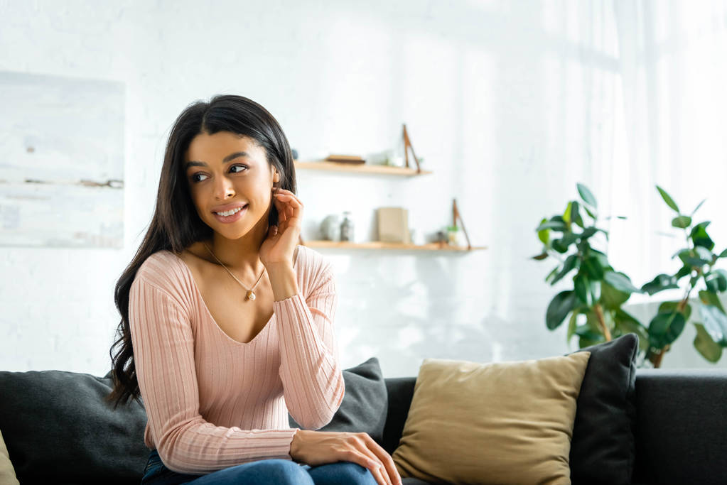 mujer afroamericana sonriente sentada en un sofá y mirando hacia otro lado
  - Foto, imagen