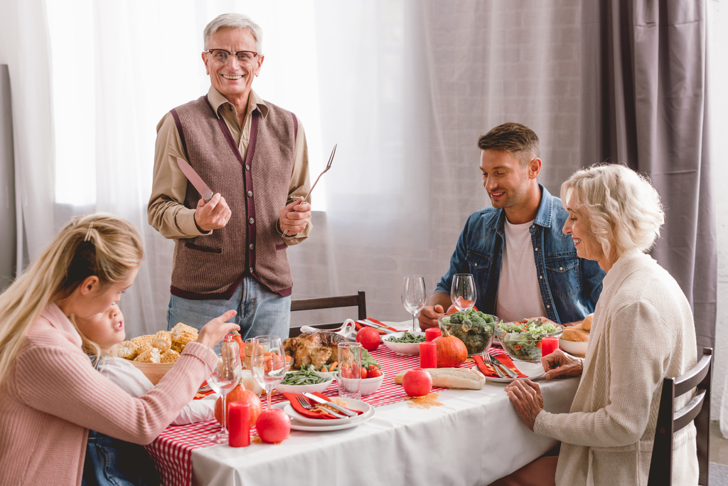 rodinní příslušníci sedí u stolu a dědeček drží příbory v den Díkůvzdání       - Fotografie, Obrázek