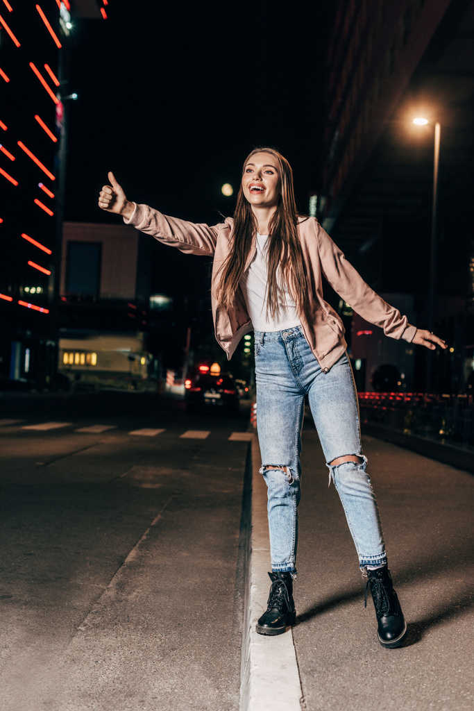 attractive woman in pink jacket hitching and smiling in night city  - Photo, Image