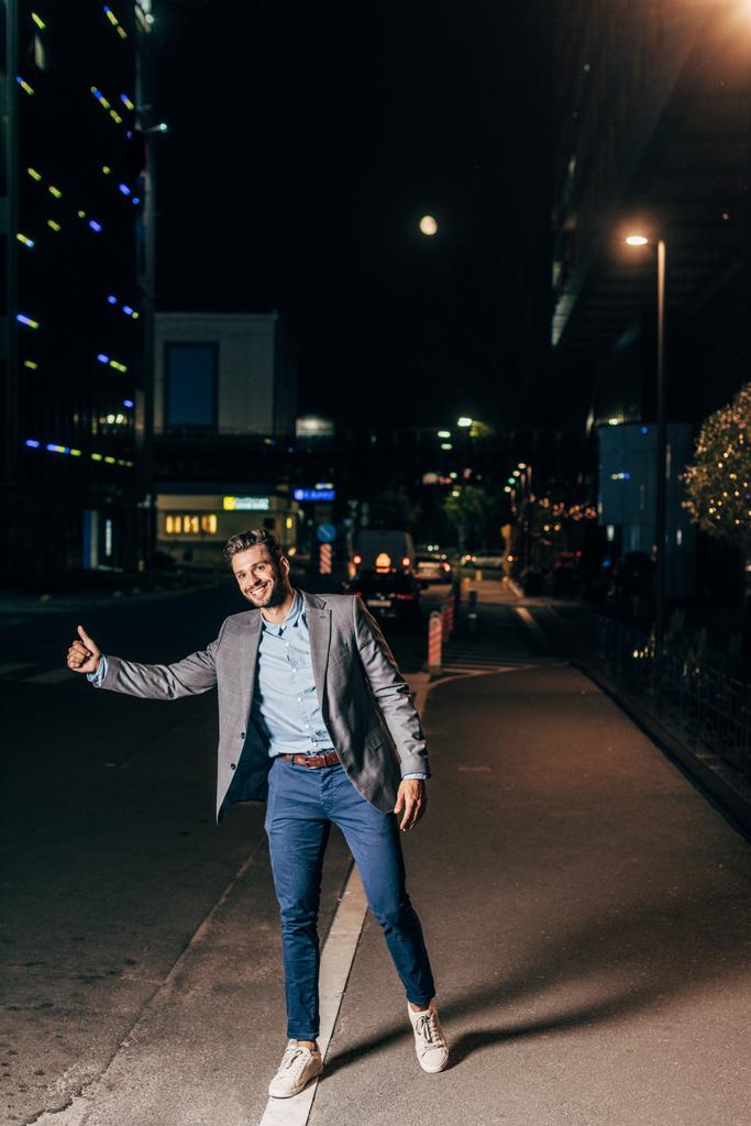 guapo hombre de negocios en ropa formal sonriente y pulgar en la ciudad de la noche
  - Foto, Imagen