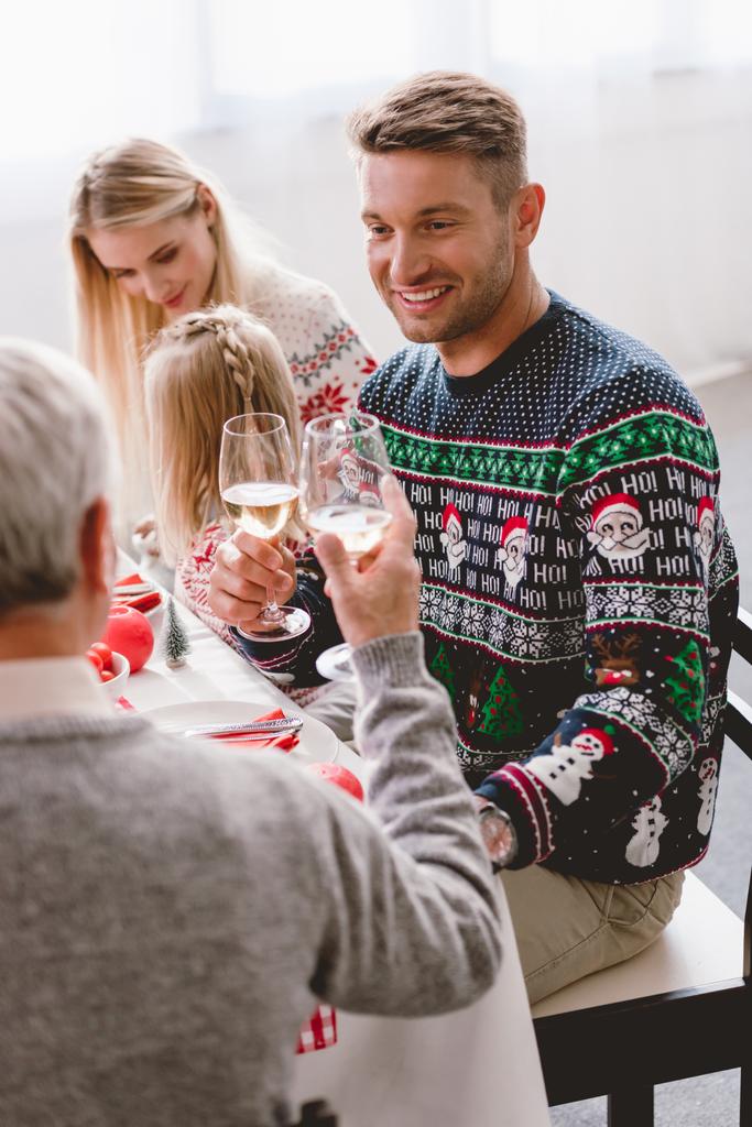 テーブルに座ってクリスマスにワイングラスでクリンクする家族の選択的な焦点  - 写真・画像
