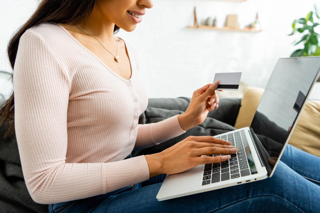 przycięte widok uśmiechnięta African American kobieta posiadania karty kredytowej i za pomocą laptopa  - Zdjęcie, obraz