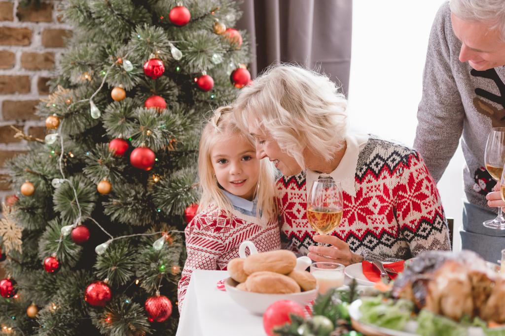 grootouders houden wijnglazen en knuffelen kleindochter in Kerstmis  - Foto, afbeelding