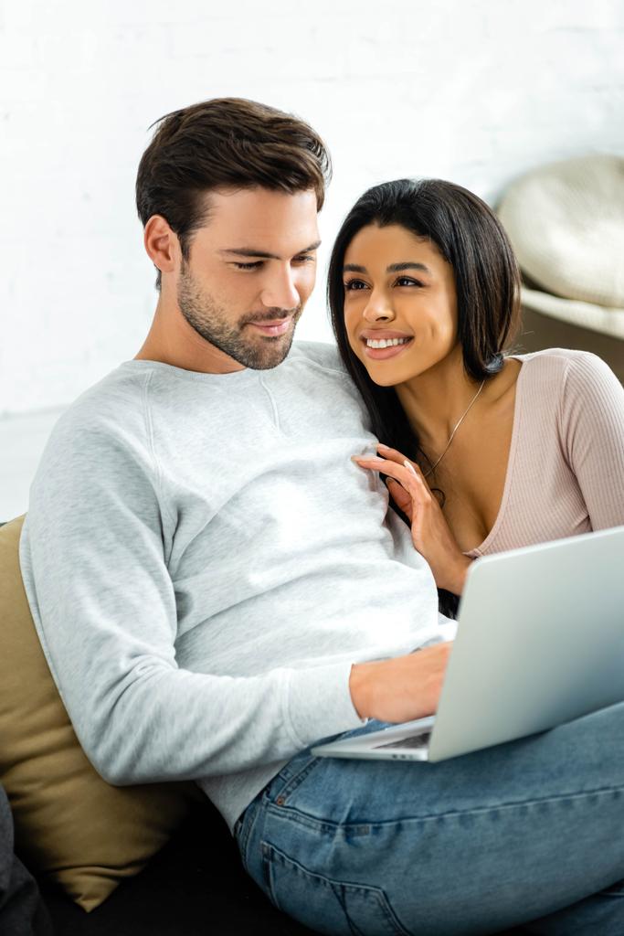 uśmiechnięta African American kobieta i przystojny mężczyzna patrząc na laptopa  - Zdjęcie, obraz