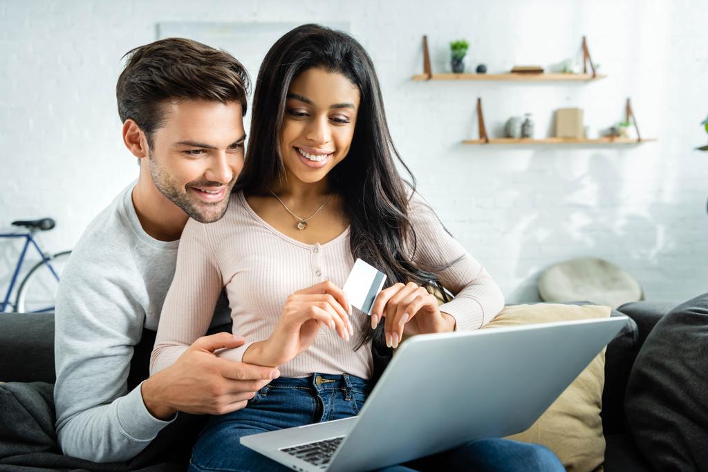 souriant afro-américaine détenant une carte de crédit et regardant ordinateur portable avec l'homme
  - Photo, image