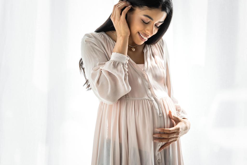 souriant enceinte afro-américaine femme étreignant ventre dans l'appartement
 - Photo, image