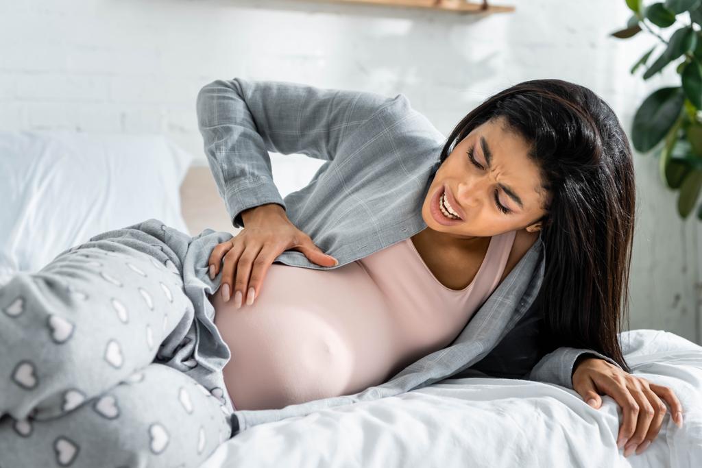 African American kobieta w ciąży w piżamie dotykając brzucha i uczucie bólu  - Zdjęcie, obraz
