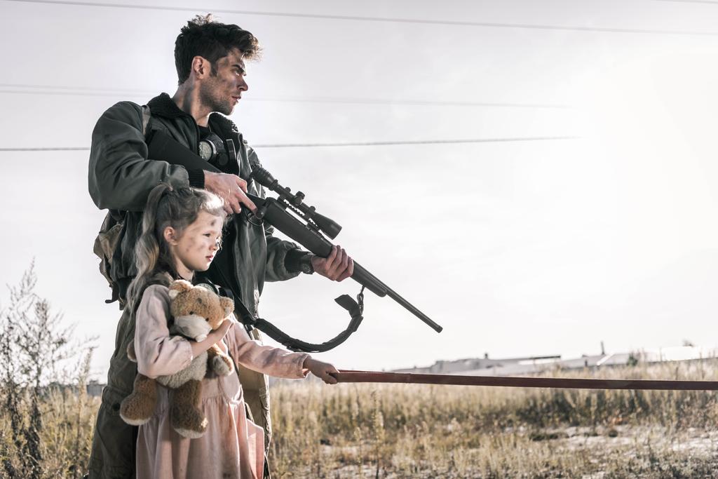 man holding gun near child with teddy bear, post apocalyptic concept - Photo, Image