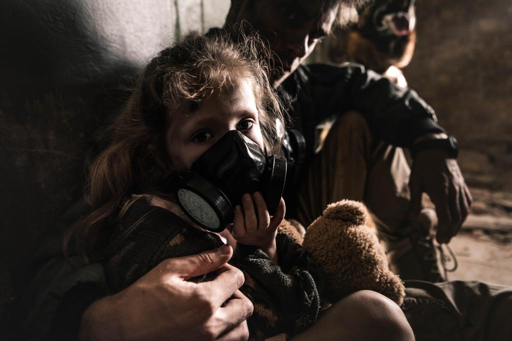 Selektiver Fokus des Mannes, der Kind in Gasmaske mit Teddybär umarmt, postapokalyptisches Konzept - Foto, Bild