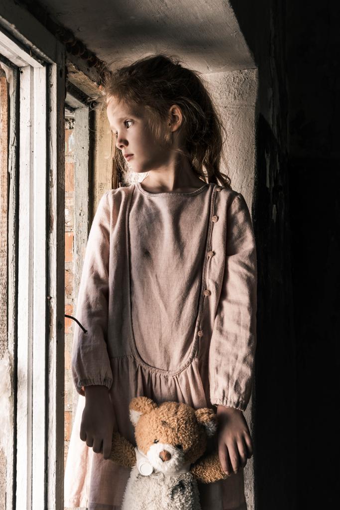 sfrustrowane dziecko trzyma pluszowego misia w pobliżu okna, po apokaliptycznej koncepcji - Zdjęcie, obraz