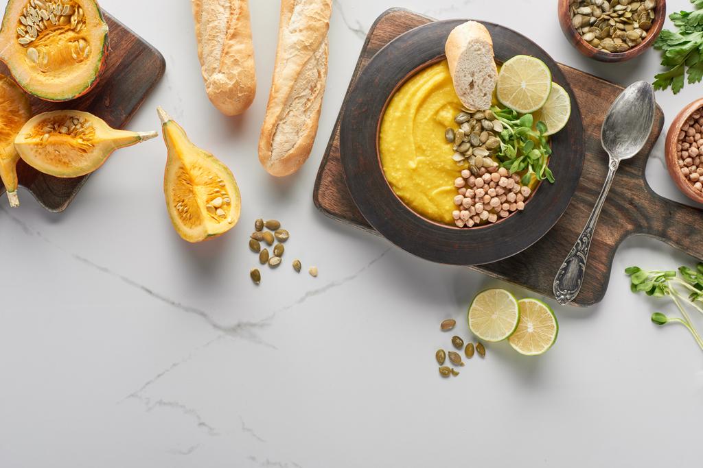 вид сверху на суп из тыквы осеннего пюре на деревянной доске возле ингредиентов и хлеб на мраморной поверхности
 - Фото, изображение