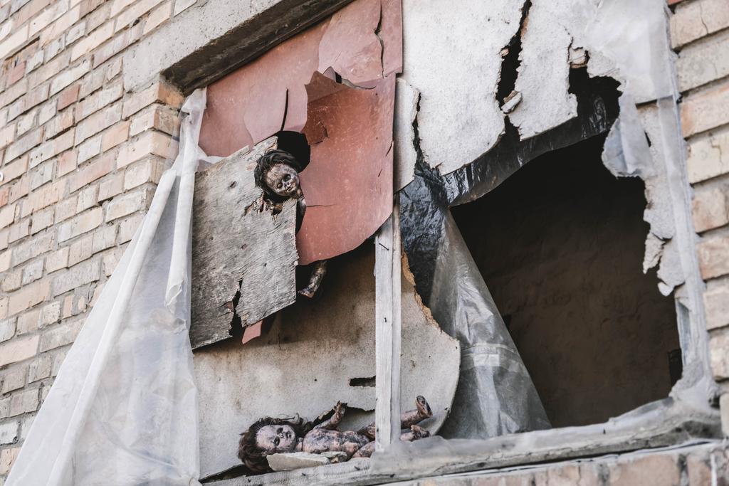eng en verbrand baby poppen in de buurt van roestige en beschadigde ramen, post apocalyptische concept - Foto, afbeelding