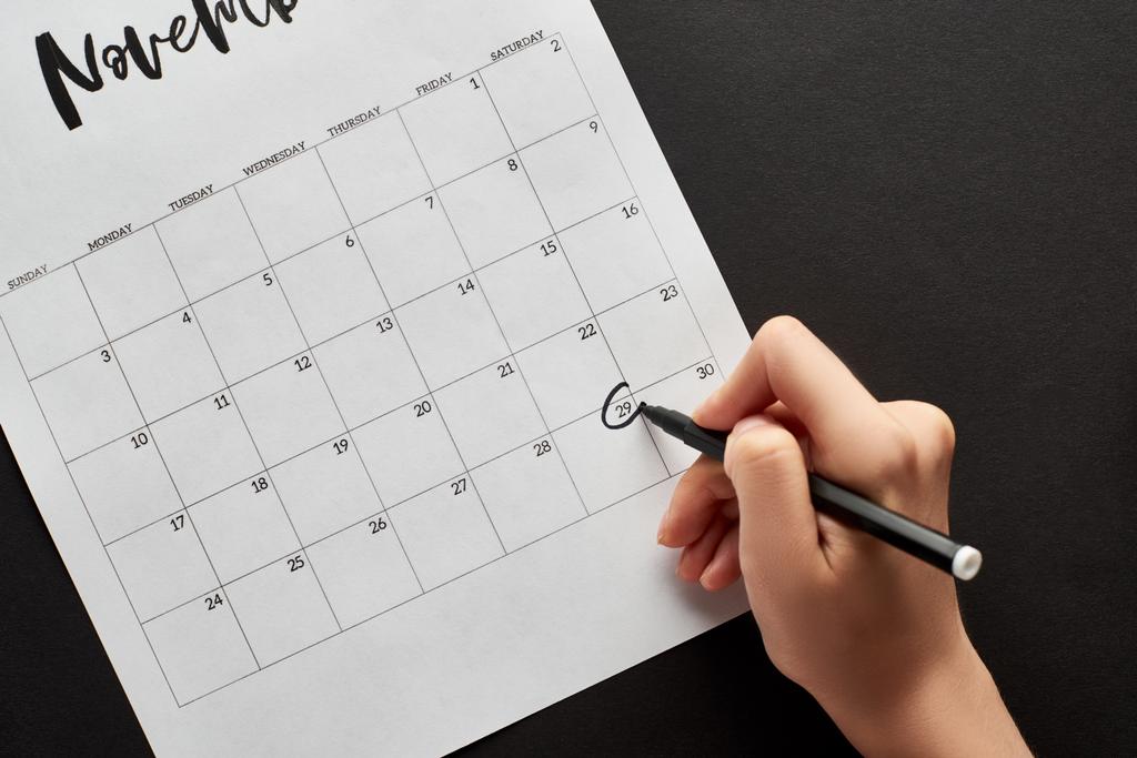 bijgesneden weergave van vrouw markering zwart vrijdag datum in kalender op zwarte achtergrond - Foto, afbeelding
