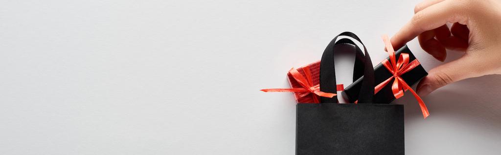 cropped view of woman putting small gift boxes in black shopping bag on white background, panoramic shot - Photo, Image