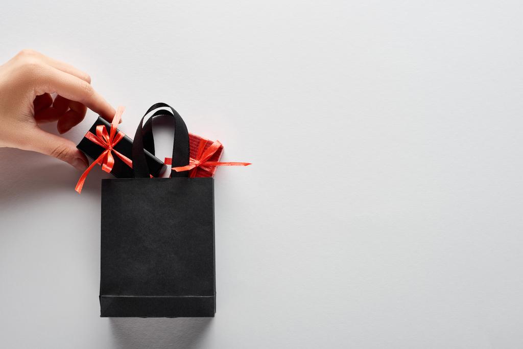 vista recortada de la mujer poniendo pequeñas cajas de regalo en negro bolsa de compras sobre fondo blanco
 - Foto, Imagen