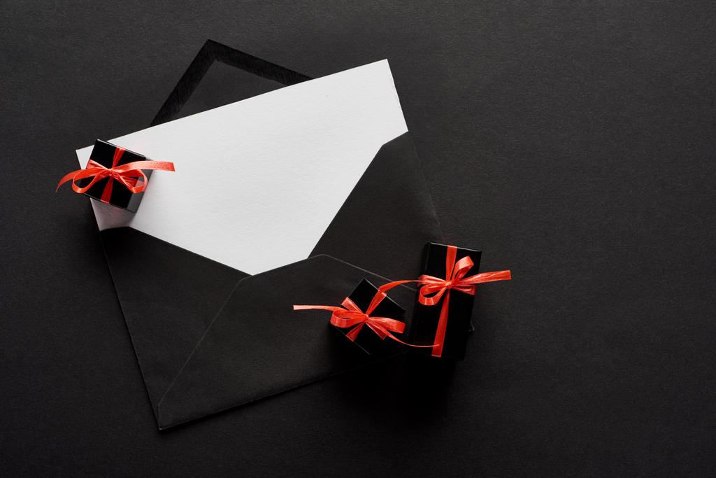top view of black envelope with blank card near decorative gift boxes on black background - Photo, Image